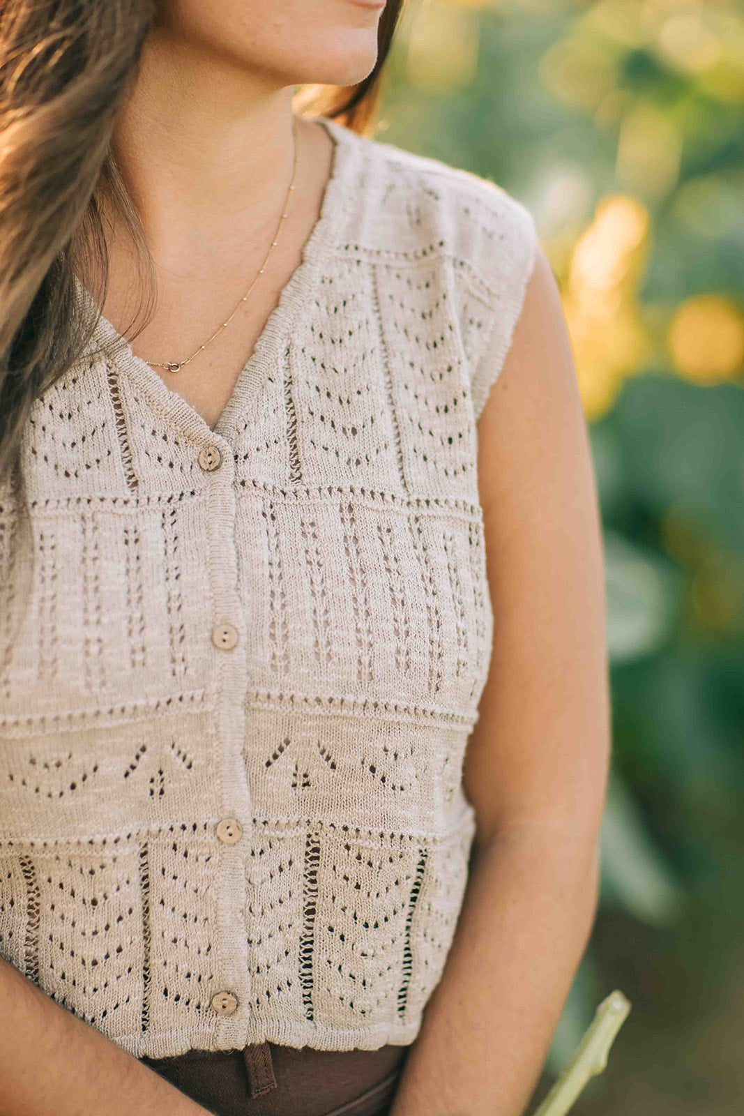 Woman wearing a beige knit vest with a blurred natural background