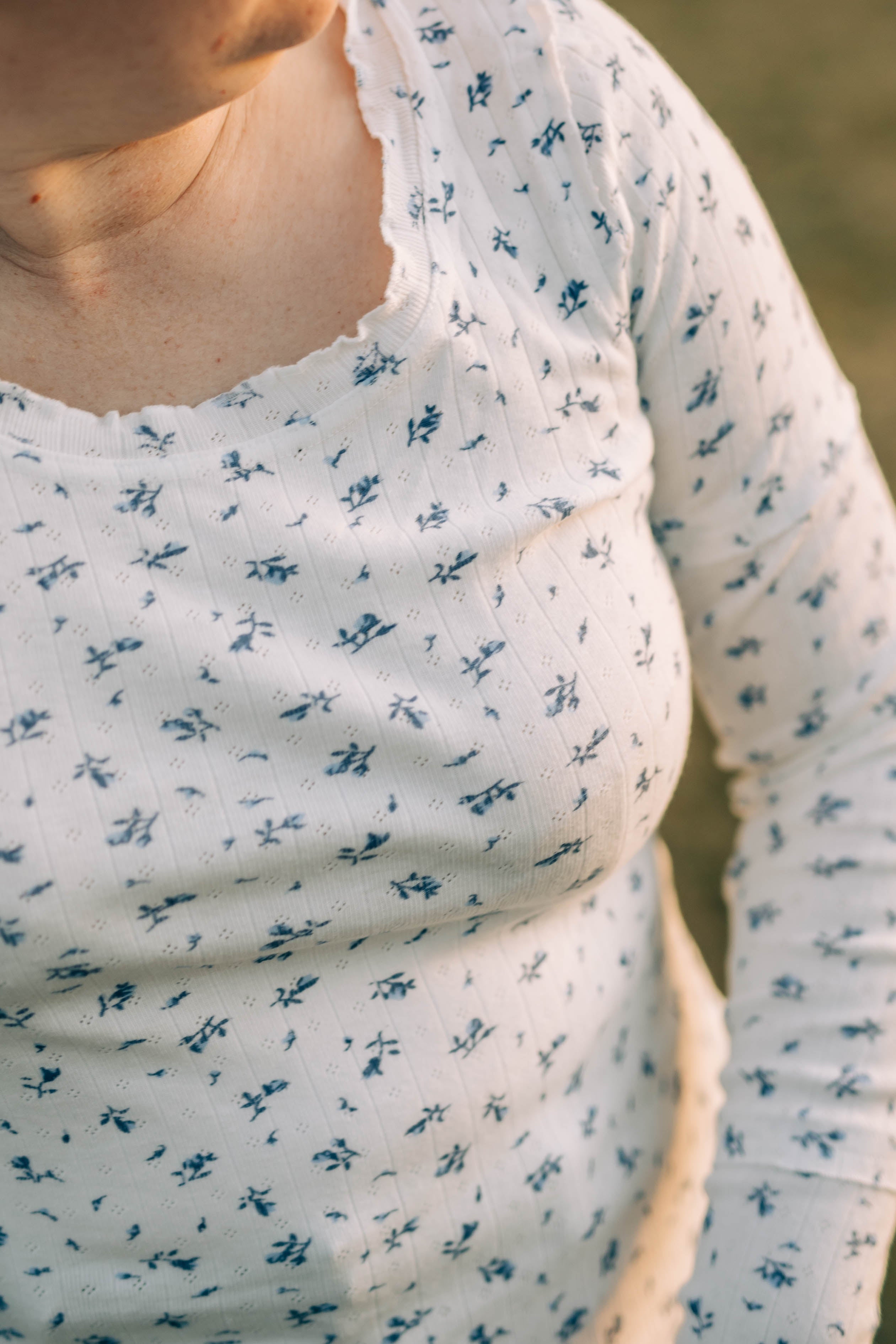 Close up of the Chelsea shirt, sold by Shop Dahl, a knit long sleeve white t-shirt with small blue flowers and a subtle ruffle hems. 