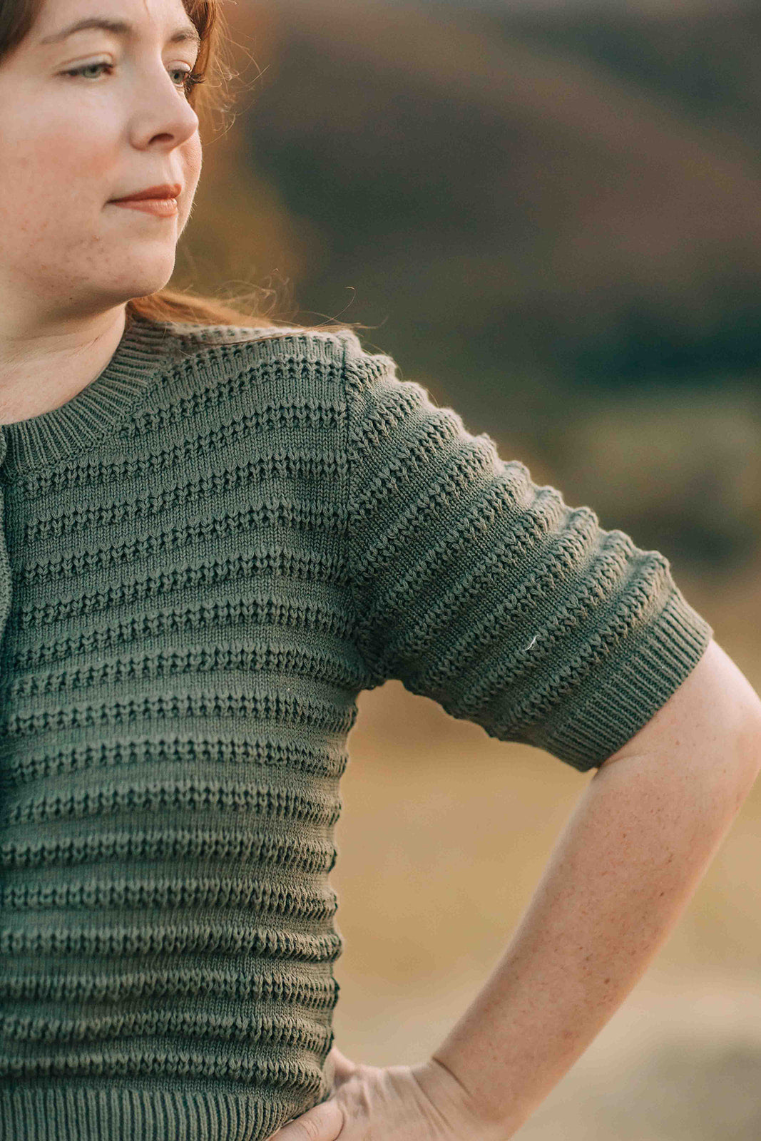 Woman wearing a green knitted sweater with a blurred natural background