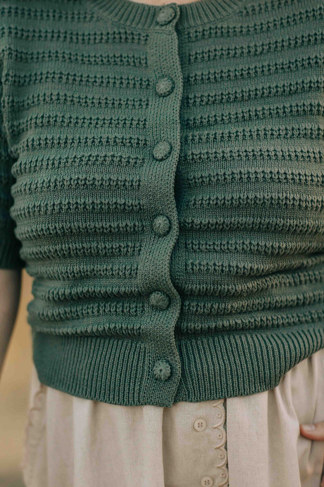 Close-up of a green knitted cardigan with buttons on a blurred background