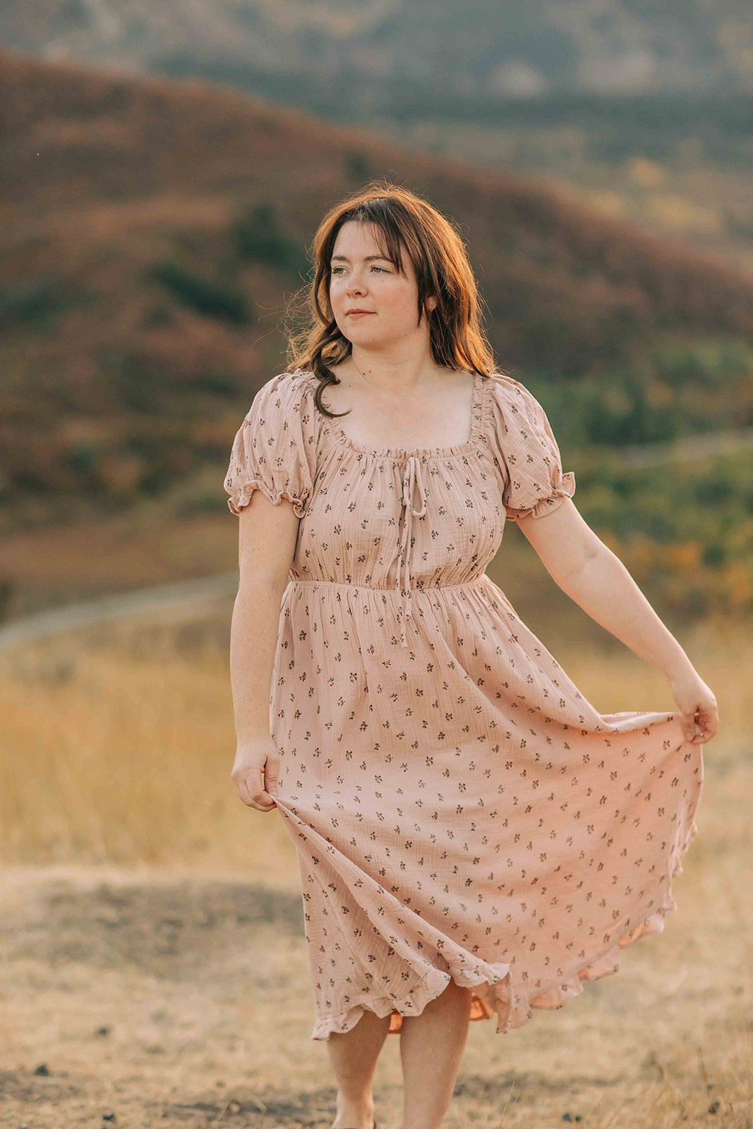 Woman wearing a dusty pink, mid calf length, short sleeve, floral dress walking up a path