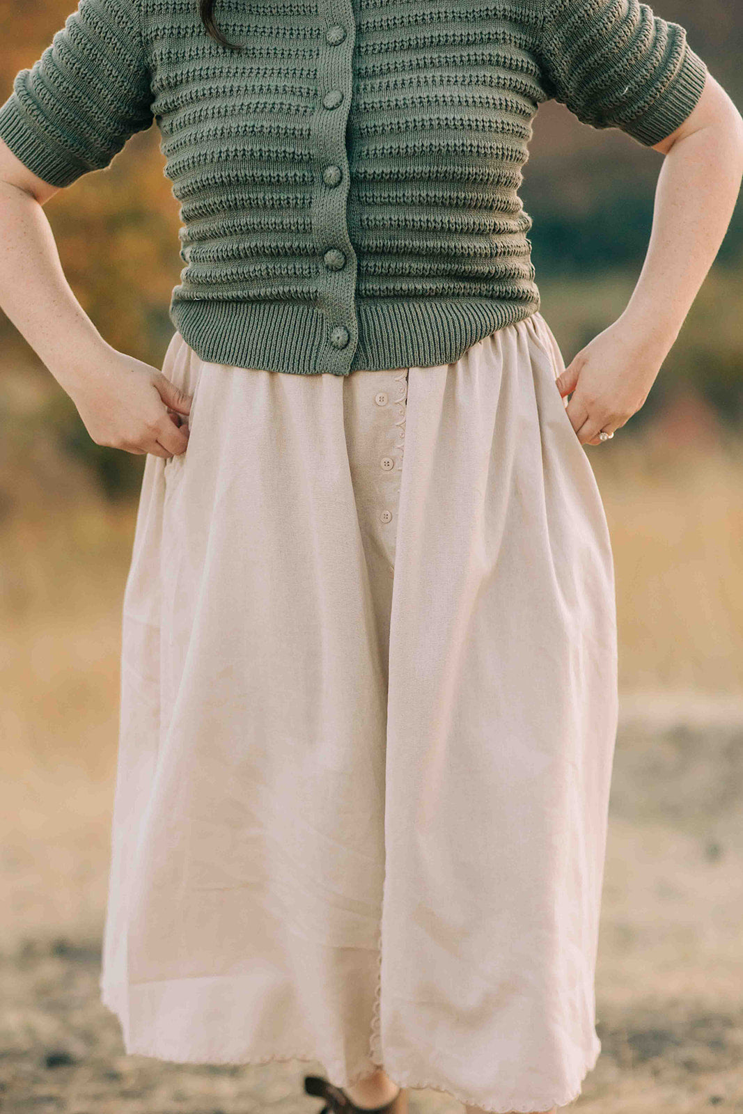 Person wearing a green knitted cardigan and beige scalloped skirt in an outdoor setting