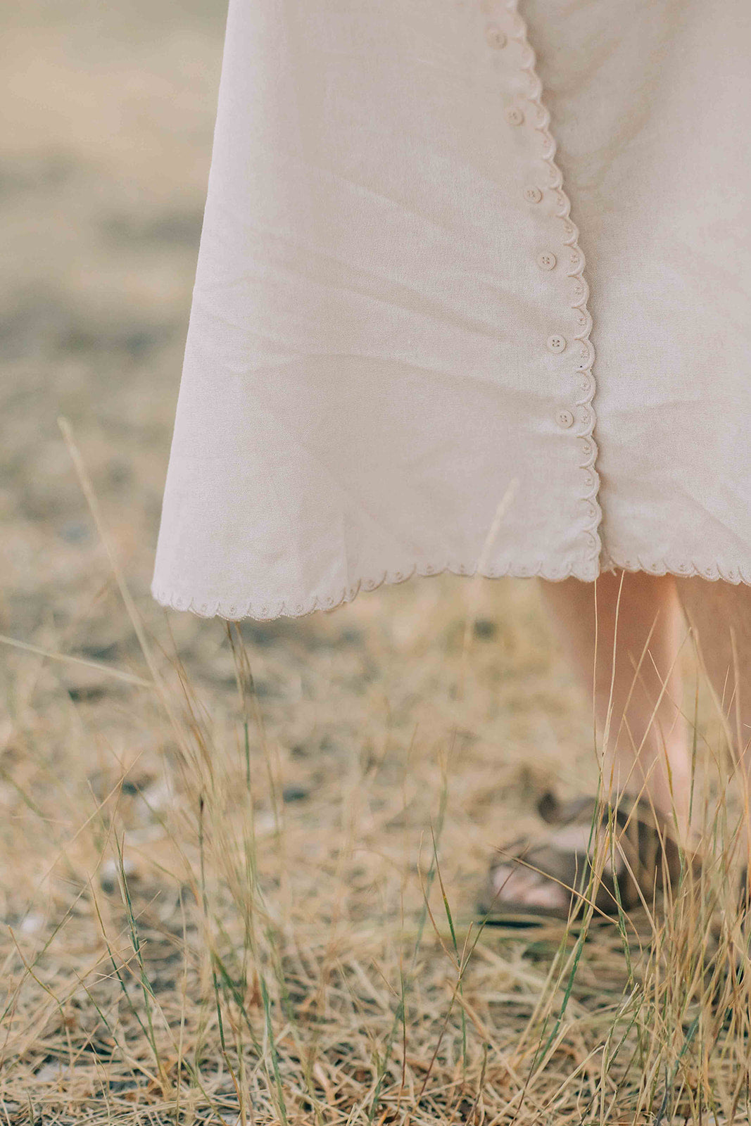 Close-up of a person wearing a beige, button down skirt, with a scalloped trim in a natural setting.