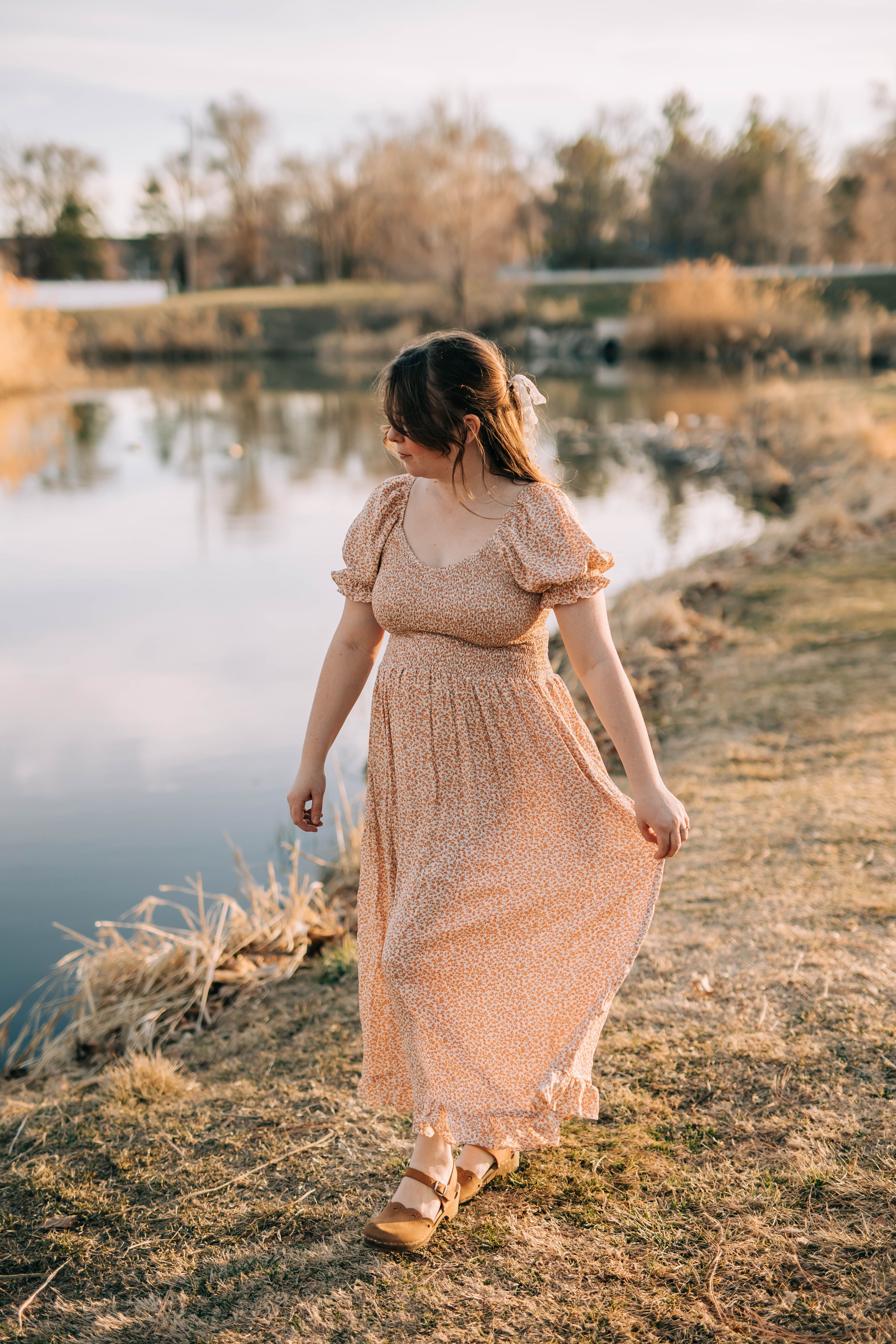 Model wears Orchard dress which is a maxi length dress with smocked bodice, V-neck and flutter sleeves. The print of the dress has small coral flowers. 