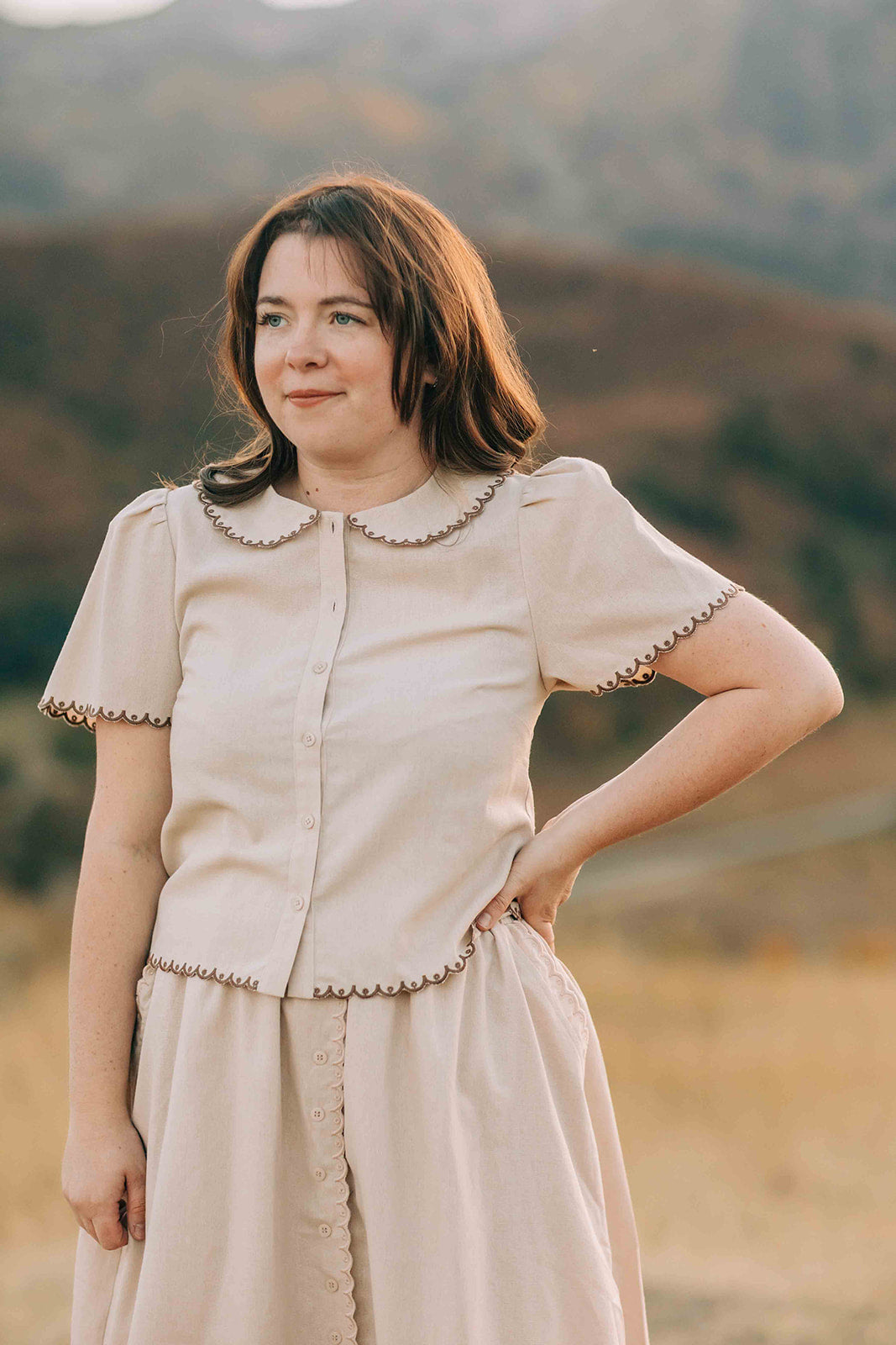 Woman in matching beige skirt an top standing outdoors with mountains in the background